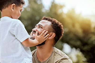Dad, boy touch face in outdoor park or backyard for summer bonding, happiness together and sunshine. Father son, happy black man in nature for love smile and quality time with child